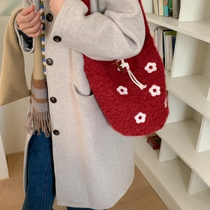 Detail of red plush bucket bag with white floral embroidery and drawstring closure