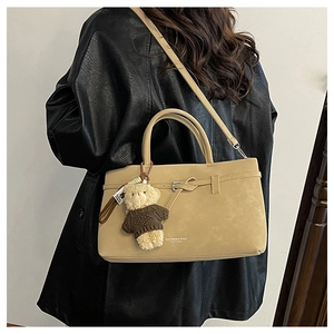 Detail view of camel tote bag with bear charm and leather strap on black leather jacket