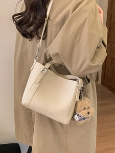 Beige lychee pattern bucket bag with dog pendant worn with a stylish trench coat