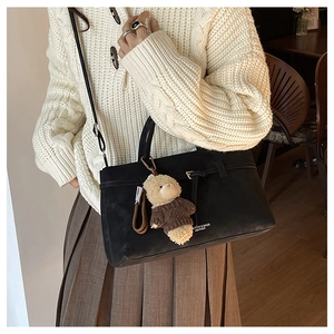 Detail of black tote bag with plush bear charm and crossbody strap on a model