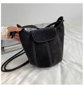 Detail of black matte leather bucket bag with contrasting white stitching and drawstring