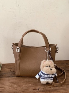 Brown litchi grain leather bucket bag with cute dog plush pendant on wood surface