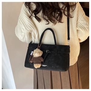 Detail of black leather handbag with cute bear charm and detachable shoulder strap