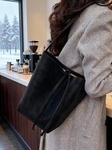 Grand sac fourre-tout noir minimaliste en daim mat porté par un mannequin dans un café