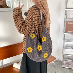 Détail du sac hobo en maille grise avec motifs de fleurs jaunes porté par un mannequin