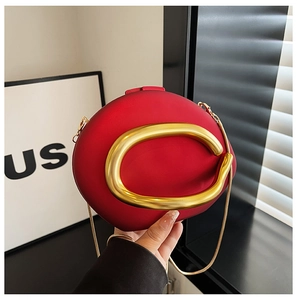 Detail of red oval evening clutch bag featuring a gold C-shaped metal handle and chain