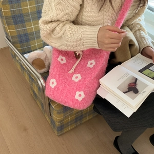 Pink plush bucket bag with floral knit pattern worn across the shoulder on a chair