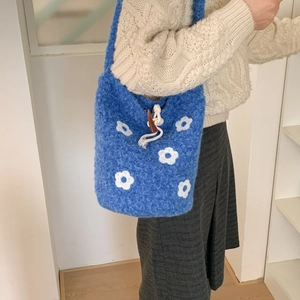 Detail of blue knit bucket bag with white daisy flowers and toggle drawstring closure