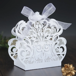 Detalle de caja de dulces blanca cortada con láser con patrón floral hueco y lazo de cinta