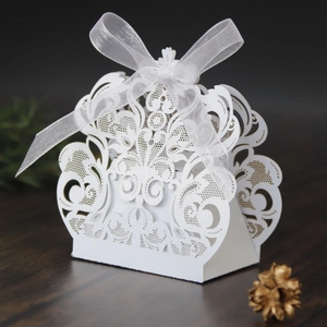 Detalle de caja de regalo blanca calada con láser y lazo de organza elegante en madera