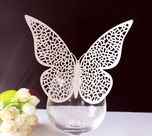 Close-up of white laser-cut butterfly cards used as decorative wedding wine glass markers