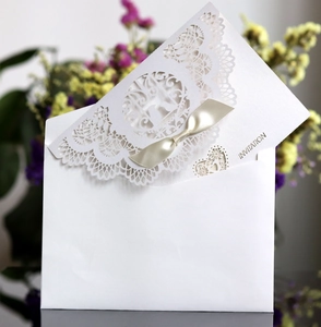 Macro shot of white laser-cut lace invitation card with elegant gold silk ribbon and envelope