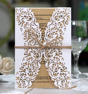 Detail of laser-cut white invitation card with twine bow and floral background