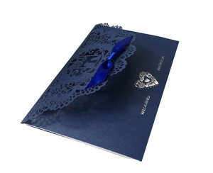 Macro detail of navy blue wedding invitation with laser-cut lace and satin ribbon bow