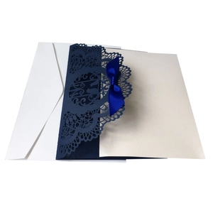 Detail of laser-cut blue lace wedding invitation with ribbon and cream inner card