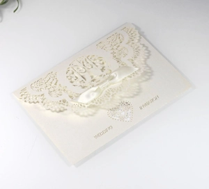 Detail of laser-cut wedding invitation card with elegant cream lace and satin bow