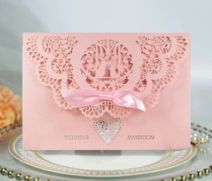 Pink laser-cut wedding invitation featuring a silk bow and pearl accents on a plate