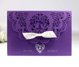 Detail view of purple laser-cut wedding invitation with white satin bow and lace pattern