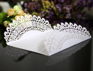 Detail of laser-cut white wedding invitation with elegant scrollwork on black surface