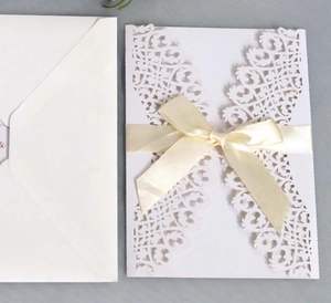 Détail d'invitation de mariage blanche découpée au laser avec nœud en satin crème