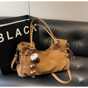 Detail of khaki leather tote bag featuring drawstring sides and a plush charm on a black sofa