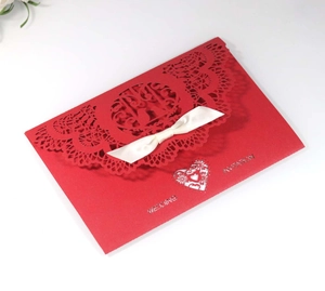 Detail view of red laser-cut wedding invitation with white ribbon and silver lettering
