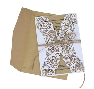 Close-up of laser-cut floral invitation with kraft inner card, twine bow, and envelope