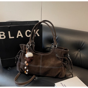 Detail of coffee brown tote bag with contrast white stitching and decorative plush pendant