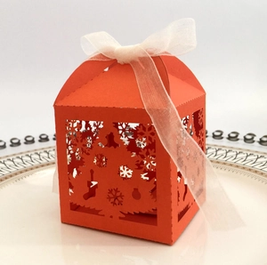 Detail of laser-cut orange Christmas candy box with snowflake patterns and white ribbon