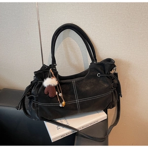 Close-up of black tote bag featuring white stitching and plush glove pendant detail