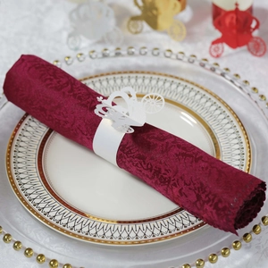 Detailed laser-cut pearl paper napkin ring in carriage shape on elegant burgundy napkin