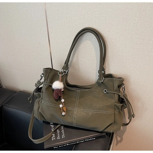 Detail of dark green tote bag featuring white contrast stitching and a plush charm detail