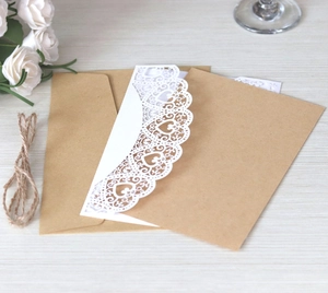 Close-up of laser-cut heart pattern wedding invitation with kraft envelope and white lace