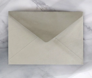 Champagne metallic pearl paper envelope with V-flap design on marble and white veil
