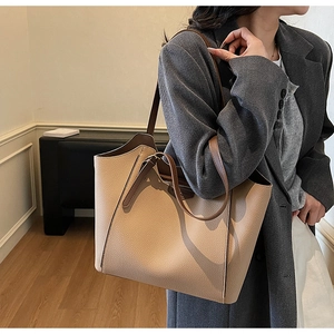 Detailed view of beige pebble leather tote bag with dark brown straps worn by model