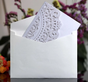 Detailed laser cut white lace wedding invitation card with matching envelope and floral decor
