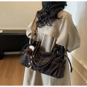 Detail of dark brown tote bag with white stitching and plush charm on a beige coat