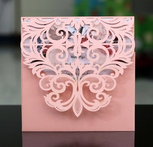 Gros plan d'une invitation rose nacrée découpée au laser avec motifs de volutes évidés