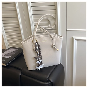 Detail of cream bucket bag with golden logo and cute schnauzer dog charm on leather bench