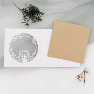 Detail view of laser-cut wedding card with floral arch design and kraft envelope