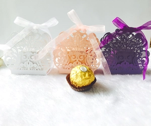 Detalle de cajas de boda cortadas por láser en blanco, rosa y morado con lazos de seda
