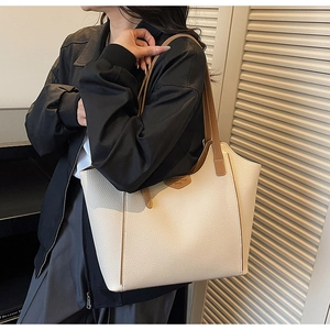 Detail shot of off-white tote bag showing pebbled leather texture and brown shoulder strap