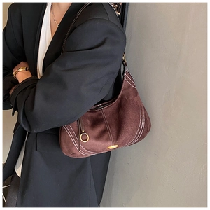 Detail of dark brown suede crescent bag with white stitching and gold metal hardware