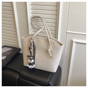 Detail of off-white leather tote bag featuring a gold logo and cute dog-shaped charm detail