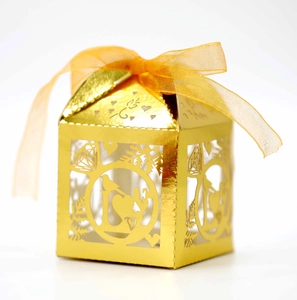 Close-up of golden hollow laser-cut wedding candy box with heart pattern and ribbon