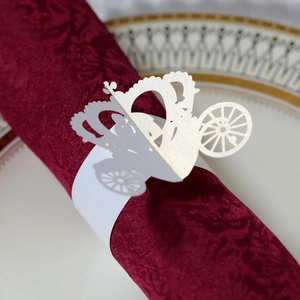 Detail of white laser-cut carriage napkin ring on a deep red damask cloth for weddings