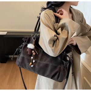 Detail of dark brown tote bag with white contrast stitching and plush glove charm