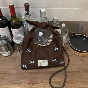 Close-up of brown suede hobo bag featuring blue ribbon bows and cream cartoon patch