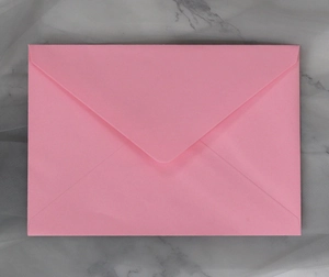 Detailed top view of a classic pink paper envelope with a V-shaped flap on marble surface