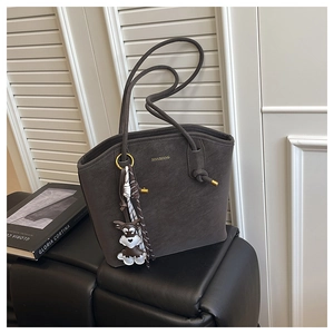 Detail of dark matte leather bucket bag featuring a golden logo and cute dog charm